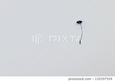 Close up detail of lone electrical wire hanging from white ceiling during house renovation. minimal construction scene shows an unfinished space with room for design Close up detail of lone electrical wire hanging from white ceiling during house renovation. minimal construction scene shows an unfinished space with room for design 130397504