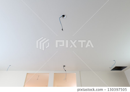 Detail view of electrical wiring hanging from ceiling during house renovation. construction project shows exposed wires for future lighting in clean white room Detail view of electrical wiring hanging from ceiling during house renovation. construction project shows exposed wires for future lighting in clean white room 130397505
