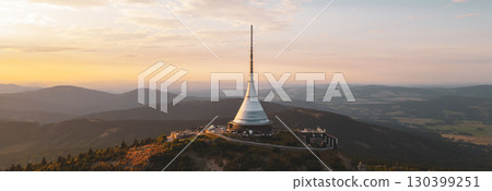 Jested Mountain Hotel stands majestically on Jested in Liberec during a sunny evening. The modern architecture glows in the warm sunset, surrounded by picturesque mountains and valleys. 130399251