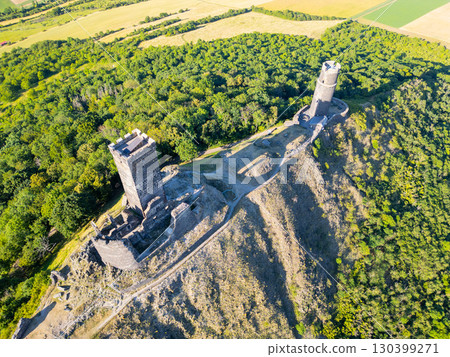 Perched atop a hill, the ruins of Hazmburk Castle showcase medieval architecture amidst lush greenery in Czechia's Central Bohemian Uplands, providing stunning views of the surrounding landscape. 130399271
