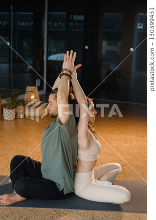 Couple practicing yoga together in a calm studio setting with warm lighting and natural decor during a serene afternoon session 130399431