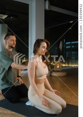 Couple practicing yoga and meditation in a tranquil studio with soft lighting during a peaceful evening session 130399432