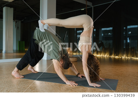 Couples practicing advanced yoga poses in a spacious indoor studio during morning light with wooden floors and large windows Couples practicing advanced yoga poses in a spacious indoor studio during morning light with wooden floors and large windows 130399439