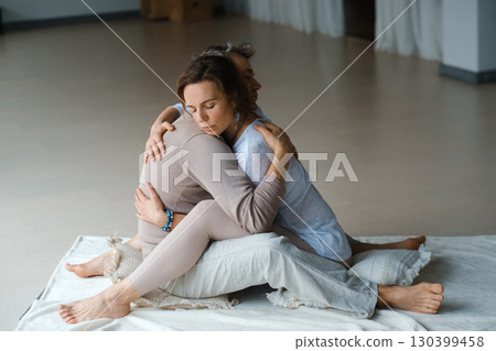 Couple engaging in a warm embrace during a morning meditation session in a bright, serene studio space 130399458