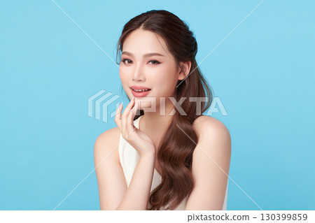 A beautiful young Asian woman with clean, fresh skin against a blue background. Skincare, facial treatment, cosmetology, beauty, and spa. An elegant portrait of an Asian woman. 130399859