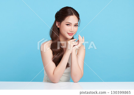 A beautiful young Asian woman with clean, fresh skin against a blue background. Skincare, facial treatment, cosmetology, beauty, and spa. An elegant portrait of an Asian woman. 130399865