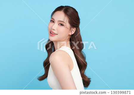 A beautiful young Asian woman with clean, fresh skin against a blue background. Skincare, facial treatment, cosmetology, beauty, and spa. An elegant portrait of an Asian woman. 130399871