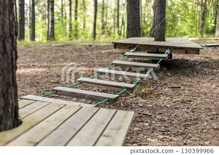 Wooden platforms and ropes create an inviting climbing experience in a serene forest. The area showcases nature's beauty while offering engaging outdoor challenges 130399966