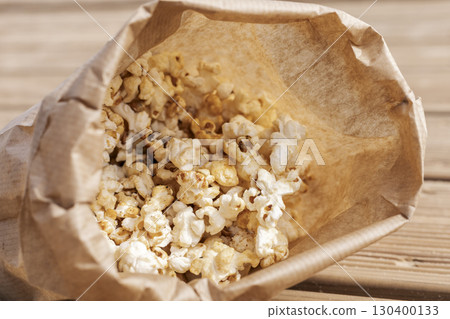 A bag of warm, fluffy popcorn sits on a rustic wooden table, inviting movie lovers to enjoy a tasty snack. Perfect for gatherings or quiet evenings at home A bag of warm, fluffy popcorn sits on a rustic wooden table, inviting movie lovers to enjoy a tasty snack. Perfect for gatherings or quiet evenings at home 130400133