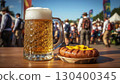 A glass of refreshing cold foamy light beer and a delicious Bavarian sausage topped with mustard. In the background are blurred people relaxing and having fun enjoying Oktoberfest, tents and flags. 130400345