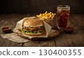 A close-up of a cheeseburger with cheddar cheese, lettuce, tomato, and a sesame seed bun, served with French fries, and a glass of iced cola on a rustic wooden table. National Cheeseburger Day 130400355