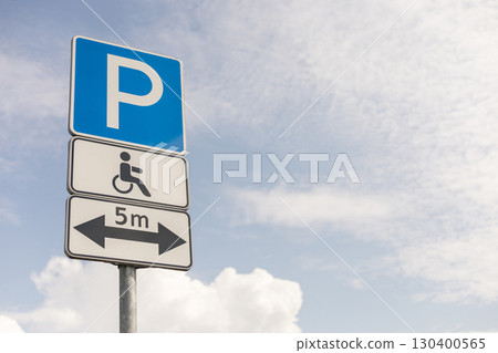 A sign displays parking regulations for accessible spaces with a wheelchair symbol, located under a clear sky, highlighting necessary parking distance 130400565