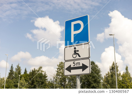 A sign displays parking regulations for accessible spaces with a wheelchair symbol, located under a clear sky, highlighting necessary parking distance 130400567