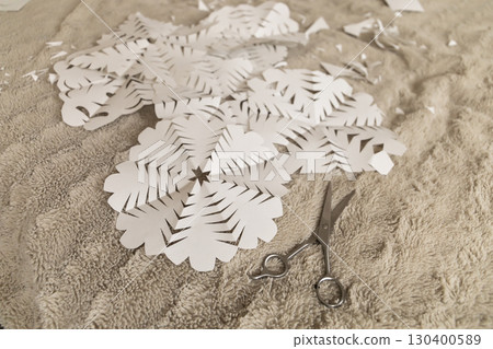 Paper snowflakes are intricately cut and scattered across a soft surface, with a pair of scissors nearby, indicating a fun crafting session during winter 130400589
