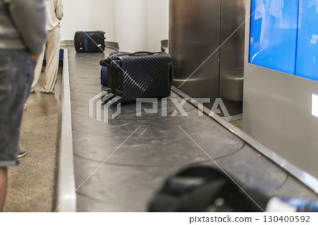 Passengers wait patiently near the luggage carousel as their bags make their way around the airport baggage claim area on a busy afternoon 130400592