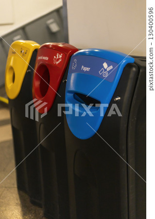 Three recycling bins are arranged in a public hallway, labeled for paper, plastic, and general waste. Each bin is color-coded: red, yellow, and blue, promoting proper disposal Three recycling bins are arranged in a public hallway, labeled for paper, plastic, and general waste. Each bin is color-coded: red, yellow, and blue, promoting proper disposal 130400596
