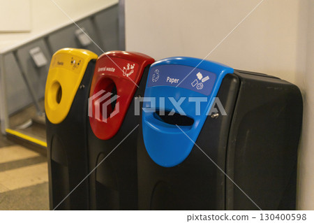 Colorful recycling bins labeled for paper, general waste, and plastic are positioned against a wall in a public space, promoting recycling and waste separation 130400598