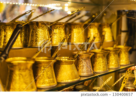 Intricately designed brass coffee pots are showcased on a glass shelf in a bustling marketplace, highlighting their ornate patterns and craftsmanship Intricately designed brass coffee pots are showcased on a glass shelf in a bustling marketplace, highlighting their ornate patterns and craftsmanship 130400657