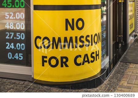 Bright yellow sign prominently displays No Commission for Cash at a financial service business. The location shows pricing information on a nearby digital board, indicating various rates 130400689