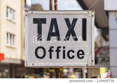 A large, clear sign reads 'Taxi Office,' indicating a location for taxi services. The setting features urban buildings and bright sunlight, capturing daily city life A large, clear sign reads 'Taxi Office,' indicating a location for taxi services. The setting features urban buildings and bright sunlight, capturing daily city life 130400736