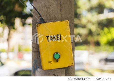 A bright yellow taxi call box is mounted on a concrete pole in a bustling city neighborhood. The green button invites commuters to summon a cab, highlighting urban mobility A bright yellow taxi call box is mounted on a concrete pole in a bustling city neighborhood. The green button invites commuters to summon a cab, highlighting urban mobility 130400757