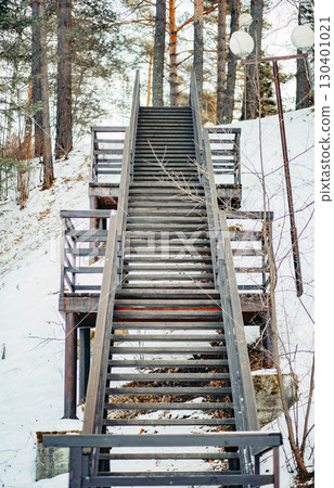 wooden staircase leading uphill through snowy forest landscape in winter season, rustic outdoor structure with railings surrounded by trees, travel, adventure and seasonal nature 130401021