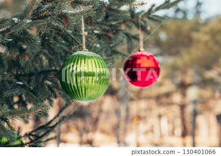 green and red Christmas baubles hanging on spruce branches outdoors in winter forest, holiday decoration concept of festive season and new year celebration green and red Christmas baubles hanging on spruce branches outdoors in winter forest, holiday decoration concept of festive season and new year celebration 130401066