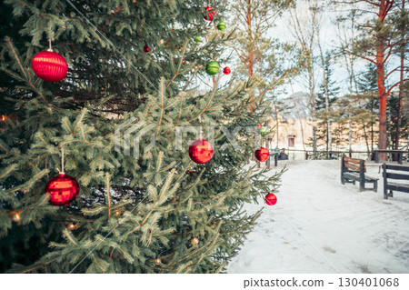 Christmas tree decorated with red and green baubles outdoors in snowy park, holiday atmosphere with festive ornaments and concept of winter celebration and new year decoration 130401068