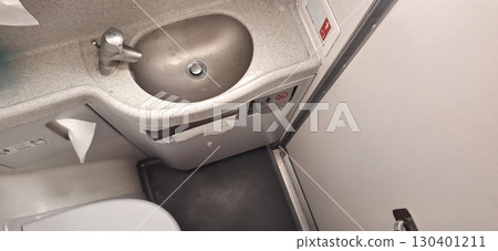 Restroom facilities onboard an airplane featuring a small sink and toilet area. The white walls and gray accents provide a functional yet limited space for passenger use 130401211