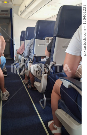 Passengers are seated in an airplane cabin, some relaxing while others check their belongings. The atmosphere is calm as the flight prepares for departure on a sunny afternoon Passengers are seated in an airplane cabin, some relaxing while others check their belongings. The atmosphere is calm as the flight prepares for departure on a sunny afternoon 130401222