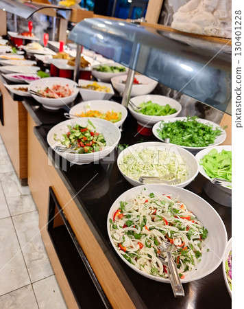 A vibrant salad bar showcases an array of fresh vegetables, including leafy greens, cucumbers, and colorful toppings, inviting diners to create their perfect salad during lunch hour 130401228