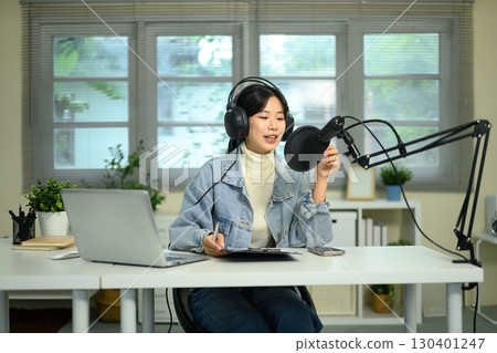 Young woman recording podcast at home studio with microphone, headphones, and laptop on desk Young woman recording podcast at home studio with microphone, headphones, and laptop on desk 130401247