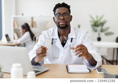 Male doctor of African descent holding medicine and water in professional office setting 130401288