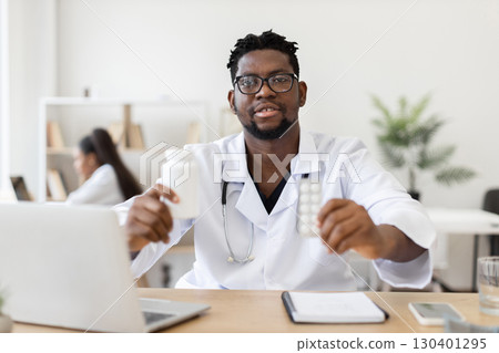 Male doctor wearing white lab coat seated in clinical office holding medication representing healthcare and medical treatment concepts. 130401295