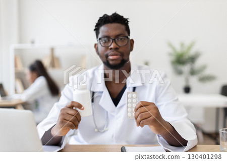 Male doctor in professional office wearing white coat holding medicine bottle and pills. Focus on healthcare, prescription medication, treatment, expertise, and modern medical environment 130401298