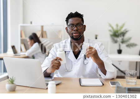 Male doctor in professional office wearing white coat holding medicine bottle and pills. Focus on healthcare, prescription medication, treatment, expertise, and modern medical environment 130401302