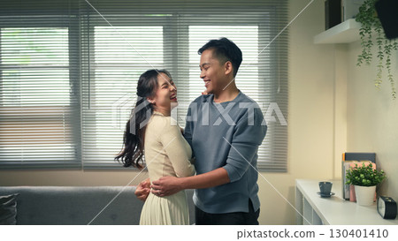 Romantic portrait of cheerful couple embracing indoors, sharing laughter and affection together 130401410