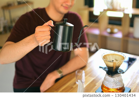 Man holding a black gooseneck kettle while brewing pour-over coffee at home 130401434