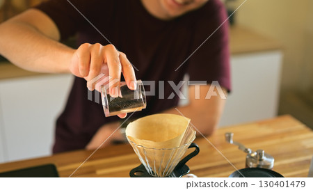 Close up of a man pouring freshly ground coffee into a paper filter for pour over brewing Close up of a man pouring freshly ground coffee into a paper filter for pour over brewing 130401479