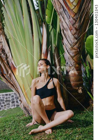 Tropical getaway young woman in black bikini sitting in front of palm tree on the beach Tropical getaway young woman in black bikini sitting in front of palm tree on the beach 130401843