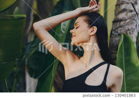 Woman in Black One Piece Swimsuit Standing in front of Palm Tree on Tropical Beach 130401863
