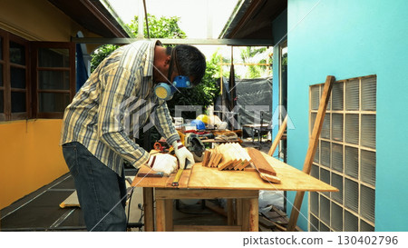 Carpenter measuring wooden plank on workbench with ruler while wearing safety mask and gloves 130402796