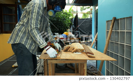 Carpenter measuring wooden plank with tape measure on workbench while wearing safety mask and gloves Carpenter measuring wooden plank with tape measure on workbench while wearing safety mask and gloves 130402797
