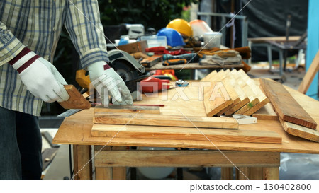 Carpenter measuring wooden plank with ruler on workbench surrounded by tools and safety equipment 130402800