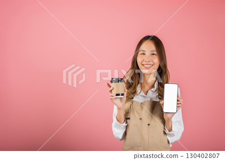 Portrait Asian happy young woman barista bar tender coffee maker holding coffee tea hot cup and mobile phone studio shot isolated on pink background, female smiling hold takeaways cup and smartphone 130402807