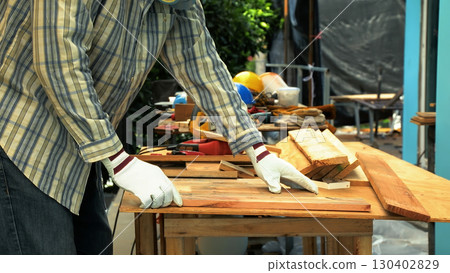 Carpenter aligning wooden planks on workbench while wearing gloves and protective gear for woodworking 130402829