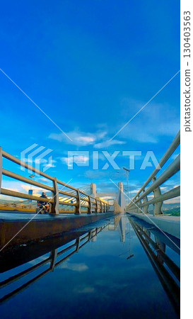 A bridge over the blue sky reflected in a puddle 130403563