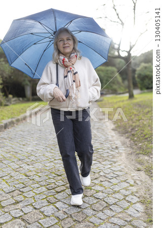 Senior woman walking in park with umbrella on cloudy day 130405141