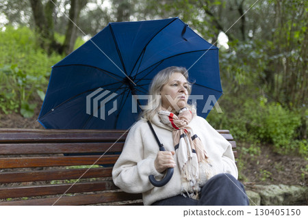 Pensive senior woman holding umbrella sitting on park bench on rainy day Pensive senior woman holding umbrella sitting on park bench on rainy day 130405150