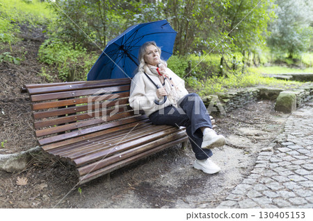 Pensive senior woman holding umbrella sitting on park bench after rain Pensive senior woman holding umbrella sitting on park bench after rain 130405153